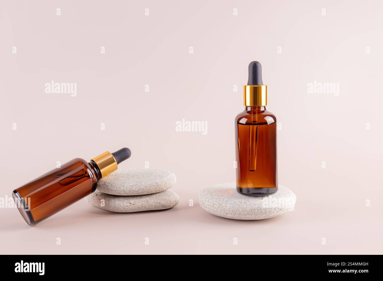 Deux flacons compte-gouttes en verre ambré sur des pierres lisses, dotés d'une esthétique minimaliste idéale pour mettre en valeur des huiles ou des produits de soin de la peau sur un dos neutre Banque D'Images