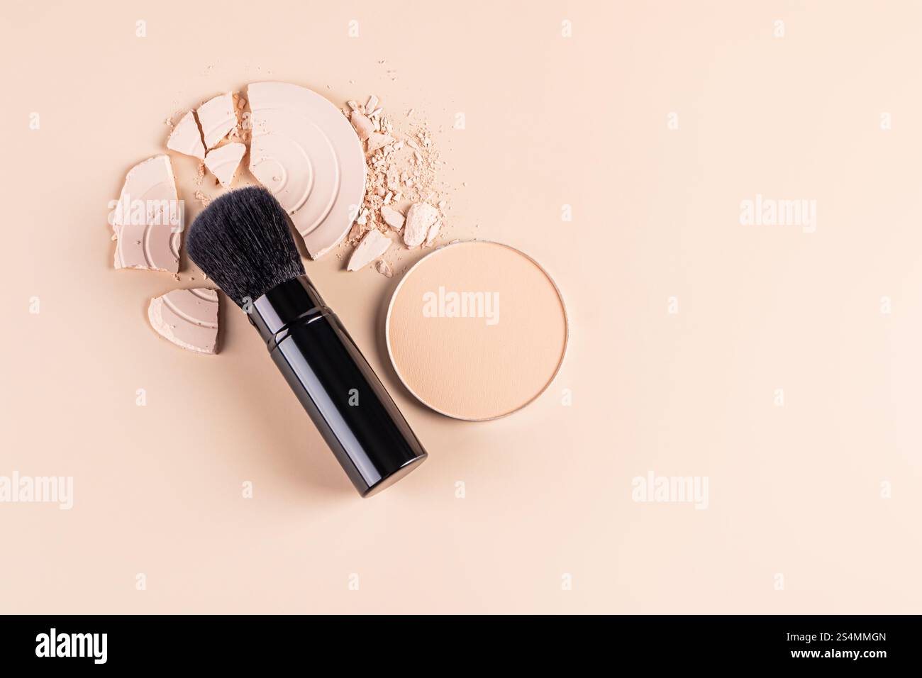 Vue de dessus d'un pinceau de maquillage à côté d'une poudre compacte pour le visage et de morceaux cassés d'une palette de poudre lâche sur un fond beige doux. Cette image capture Banque D'Images