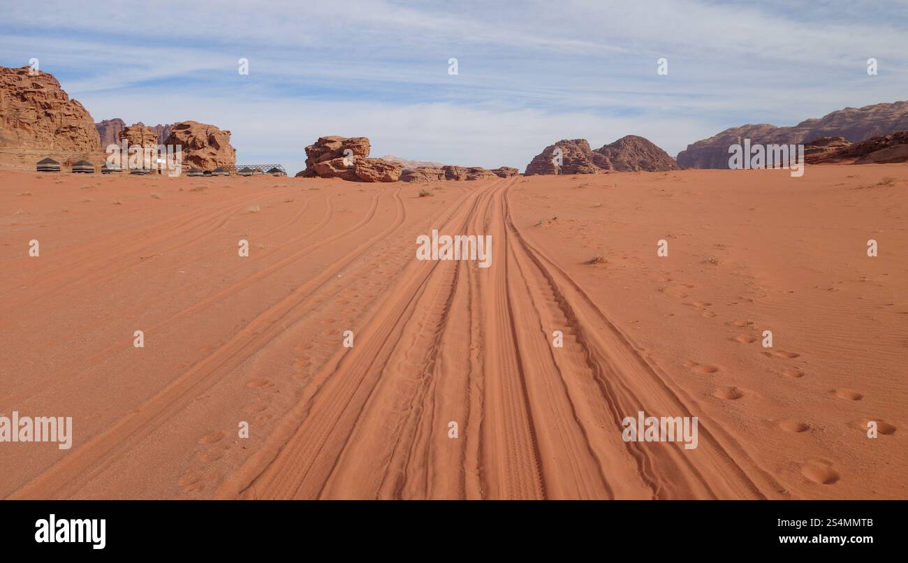Un large sentier sablonneux avec des pistes de véhicules s'étend à travers le paysage désertique à couper le souffle de Wadi Rum en Jordanie, flanqué de majestueuses formations rocheuses Banque D'Images