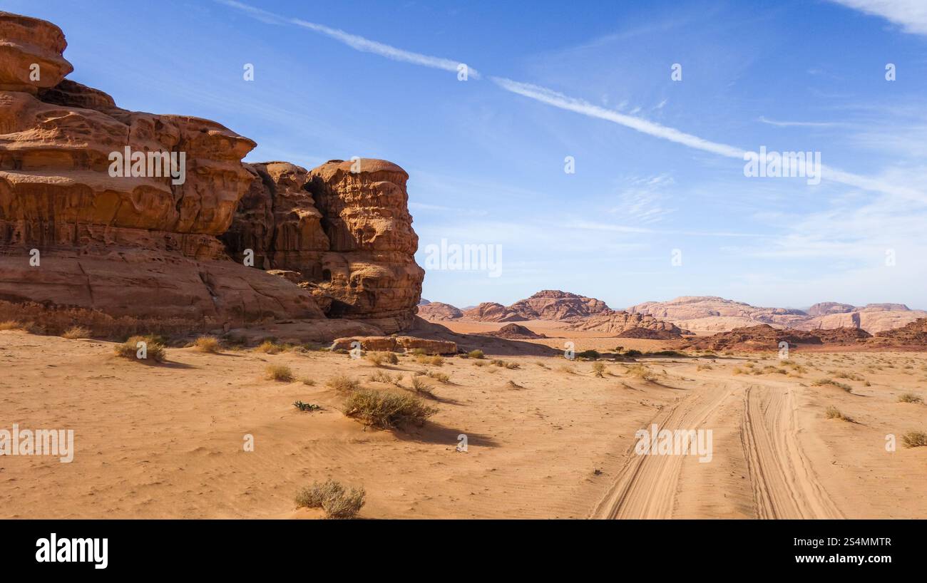 Le désert du Wadi Rum en Jordanie, avec un terrain sablonneux, des formations rocheuses et un ciel bleu clair. Un chemin de terre mène à travers le paysage fascinant, Banque D'Images