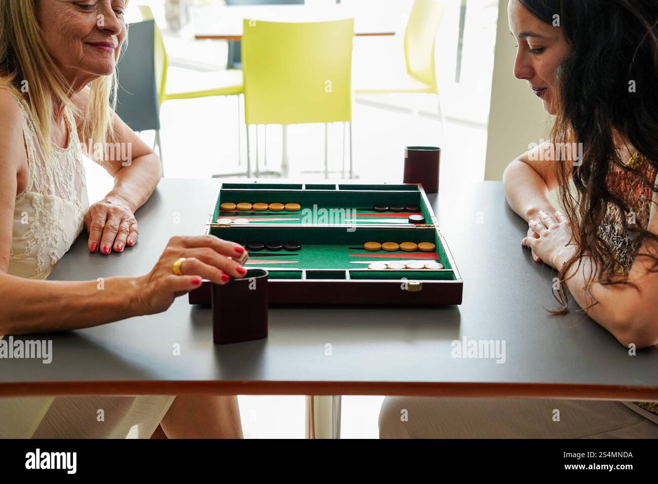 Mère et fille profiter d'un jeu de backgammon tranquille dans un café moderne la planche, avec son design classique, est posée sur une table élégante, capturant un moment Banque D'Images