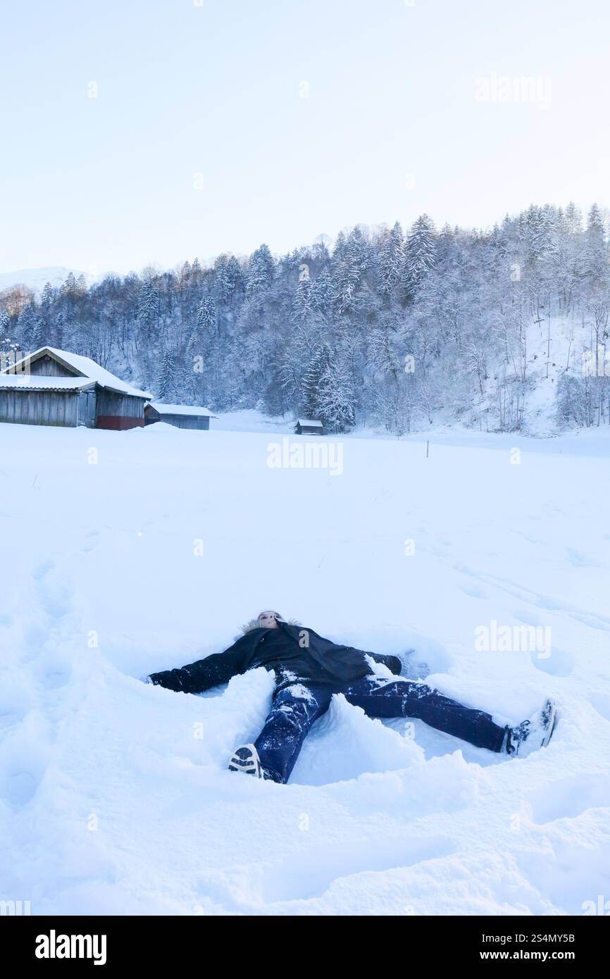 Plaisir hivernal : garçon faisant des anges de neige à la base de la montagne Banque D'Images