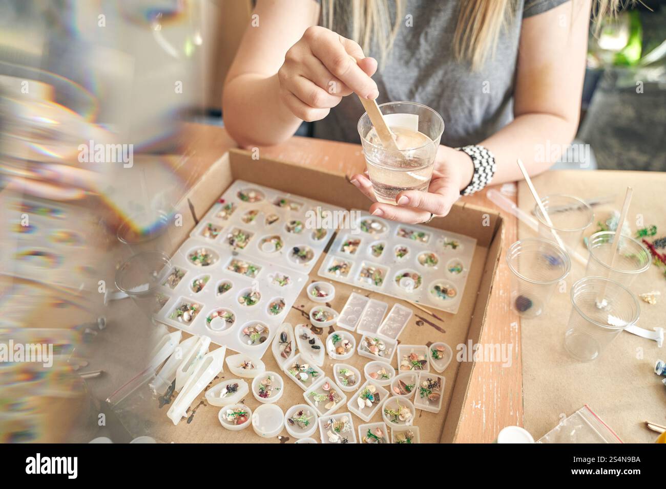 Femme artisan fabriquant des bijoux en résine avec des éléments décoratifs dans un cadre d'atelier. Banque D'Images