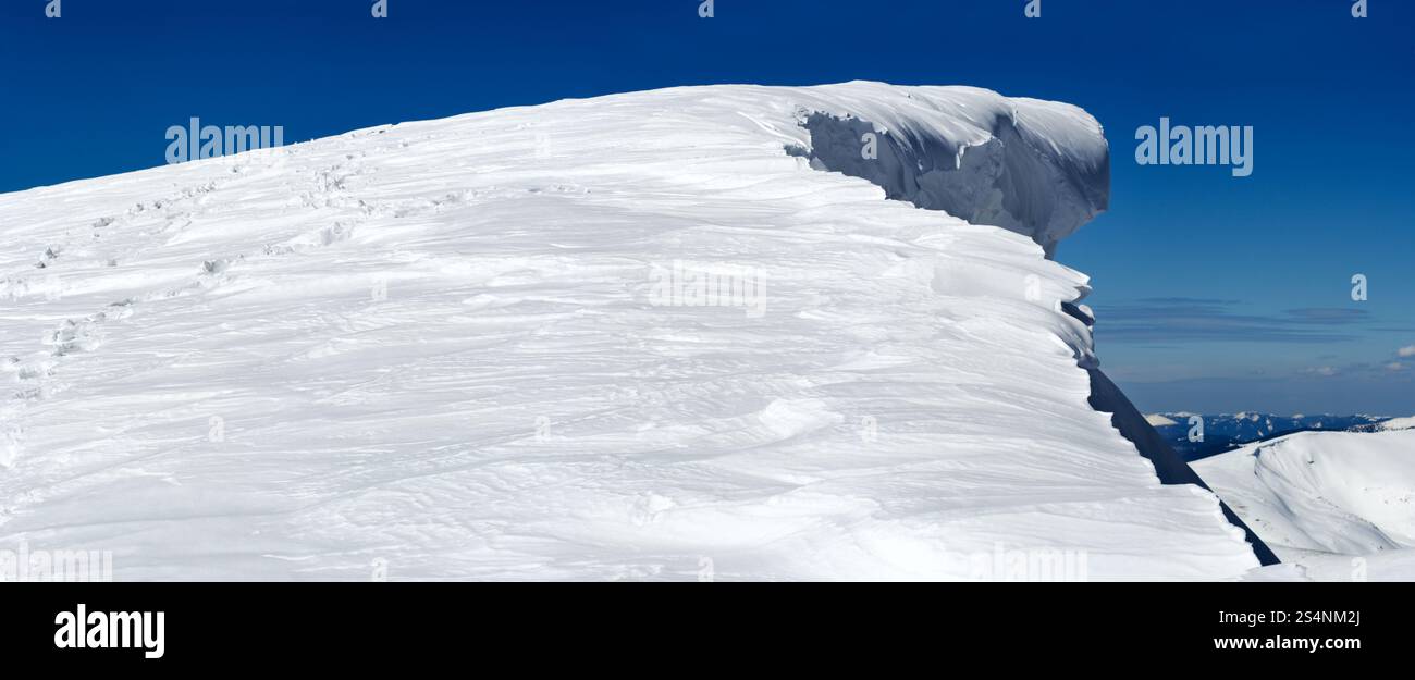 Sommet de montagne d'hiver avec chapeau de neige en surplomb de fée et empreinte humaine sur le flanc de montagne enneigé suivi d'un trépied photographique (image d'assemblage de cinq clichés) Banque D'Images