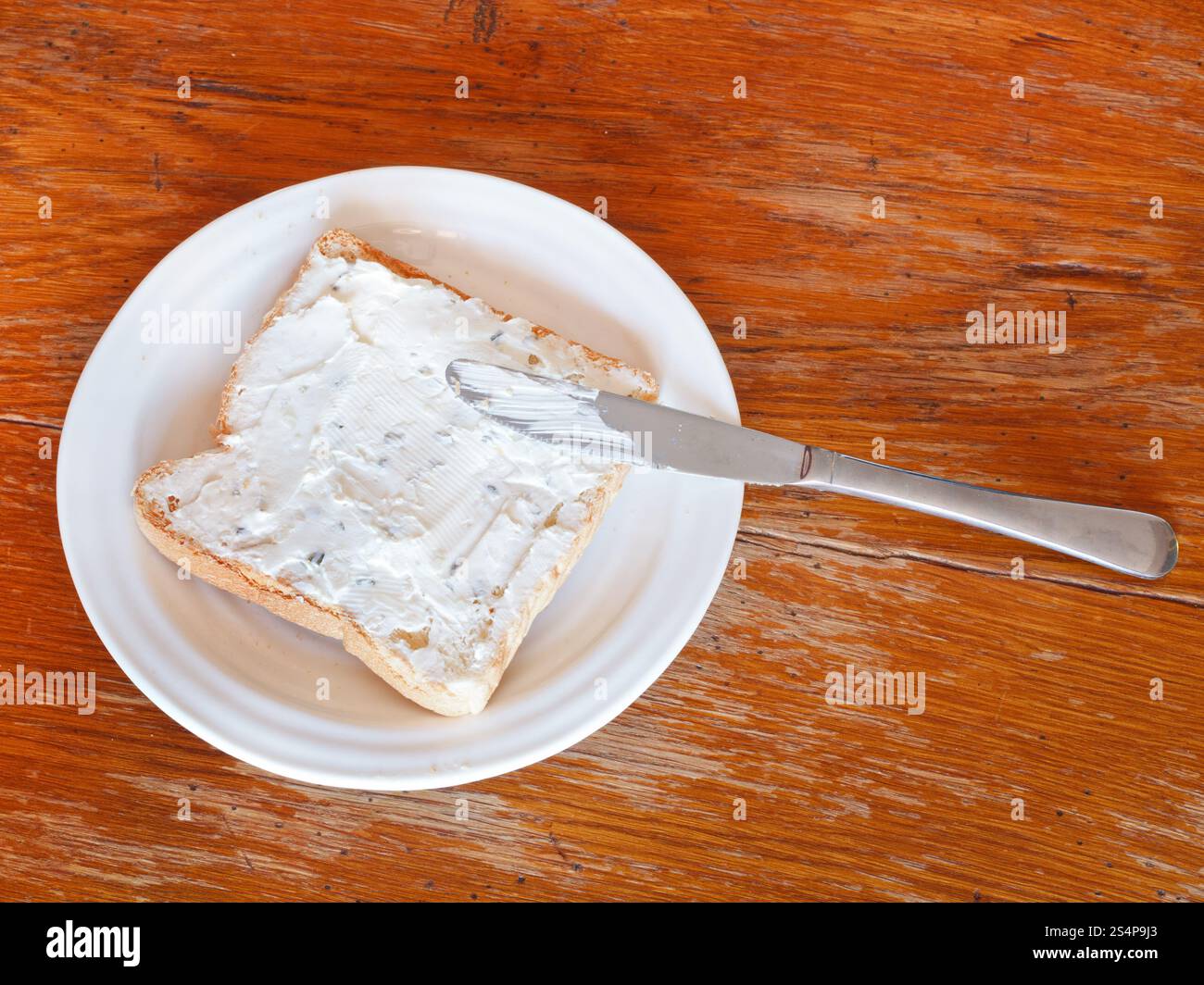 Vue de dessus du sandwich de pain grillé et fromage aux herbes sur plaque blanche, couteau de table sur une table en bois Banque D'Images