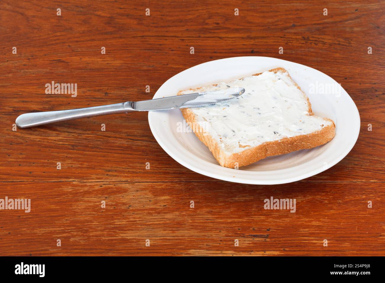 Sandwich de pain grillé et le fromage blanc aux herbes sur plaque blanche, couteau de table sur une table en bois Banque D'Images