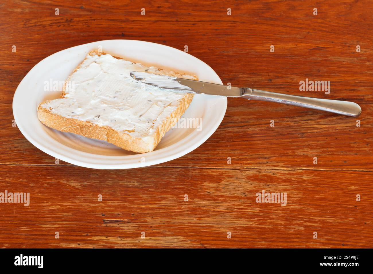 sandwich de pain grillé et fromage à pâte molle avec des herbes sur une assiette blanche, couteau de table sur une table en bois Banque D'Images