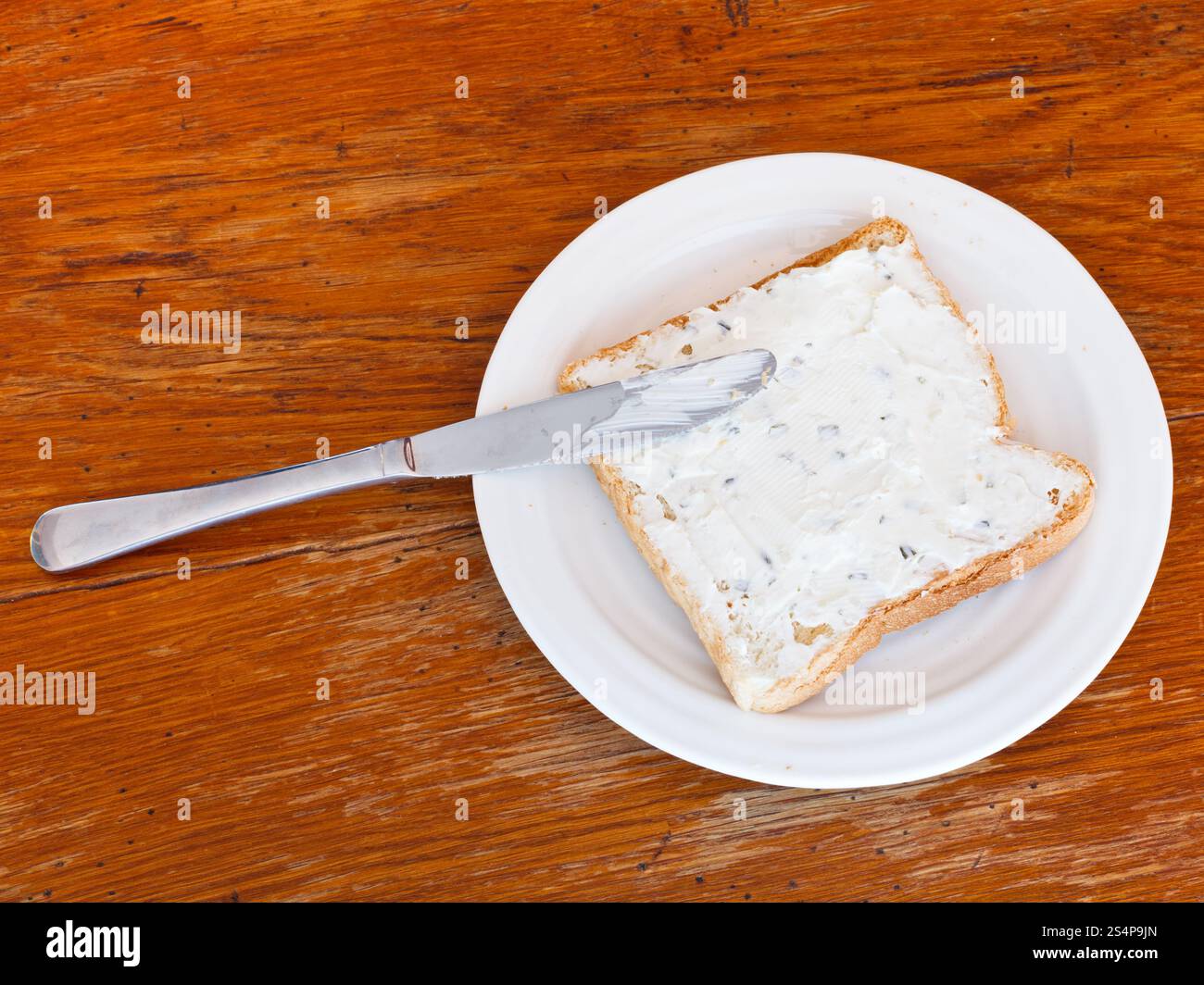 vue de dessus du sandwich de pain grillé et cottagecheese avec des herbes sur plaque blanche, couteau de table sur table en bois Banque D'Images