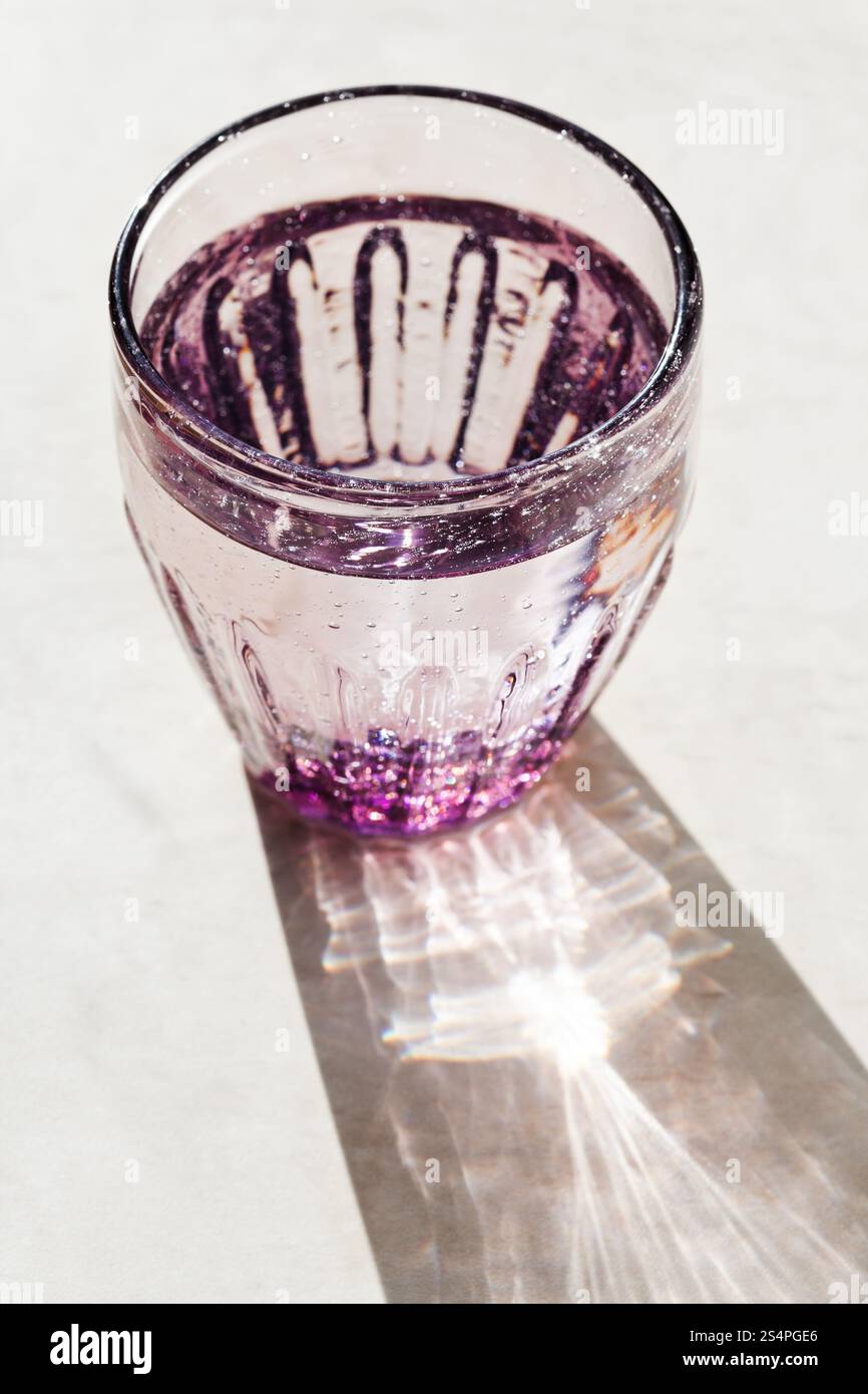 Verre à facettes violet avec de l'eau de source éclairée par la lumière du soleil Banque D'Images