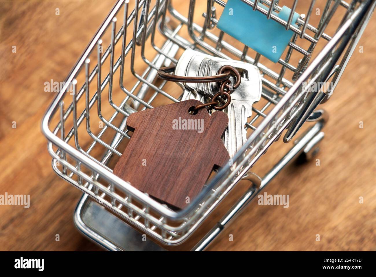 Petit chariot avec porte-clés en forme de maison en bois et clés argentées à l'intérieur. Gros plan sur une surface de tableau marron. Concept d'achat à domicile Banque D'Images