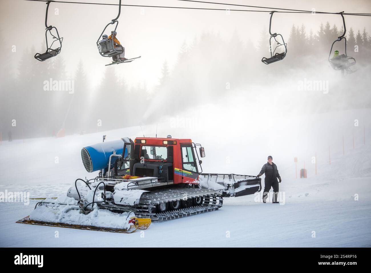 Machine de nettoyage de neige gros travail sur une piste de ski sous les chaises de câble Banque D'Images