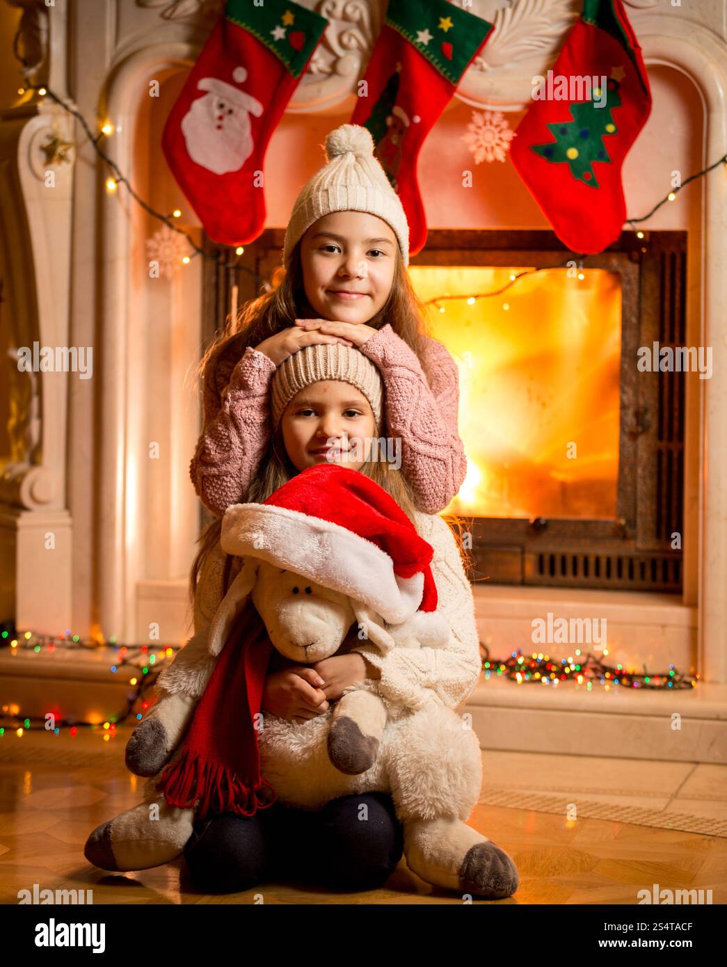 Portrait de cheminée contre smiling girls sitting on floor with toy moutons Banque D'Images