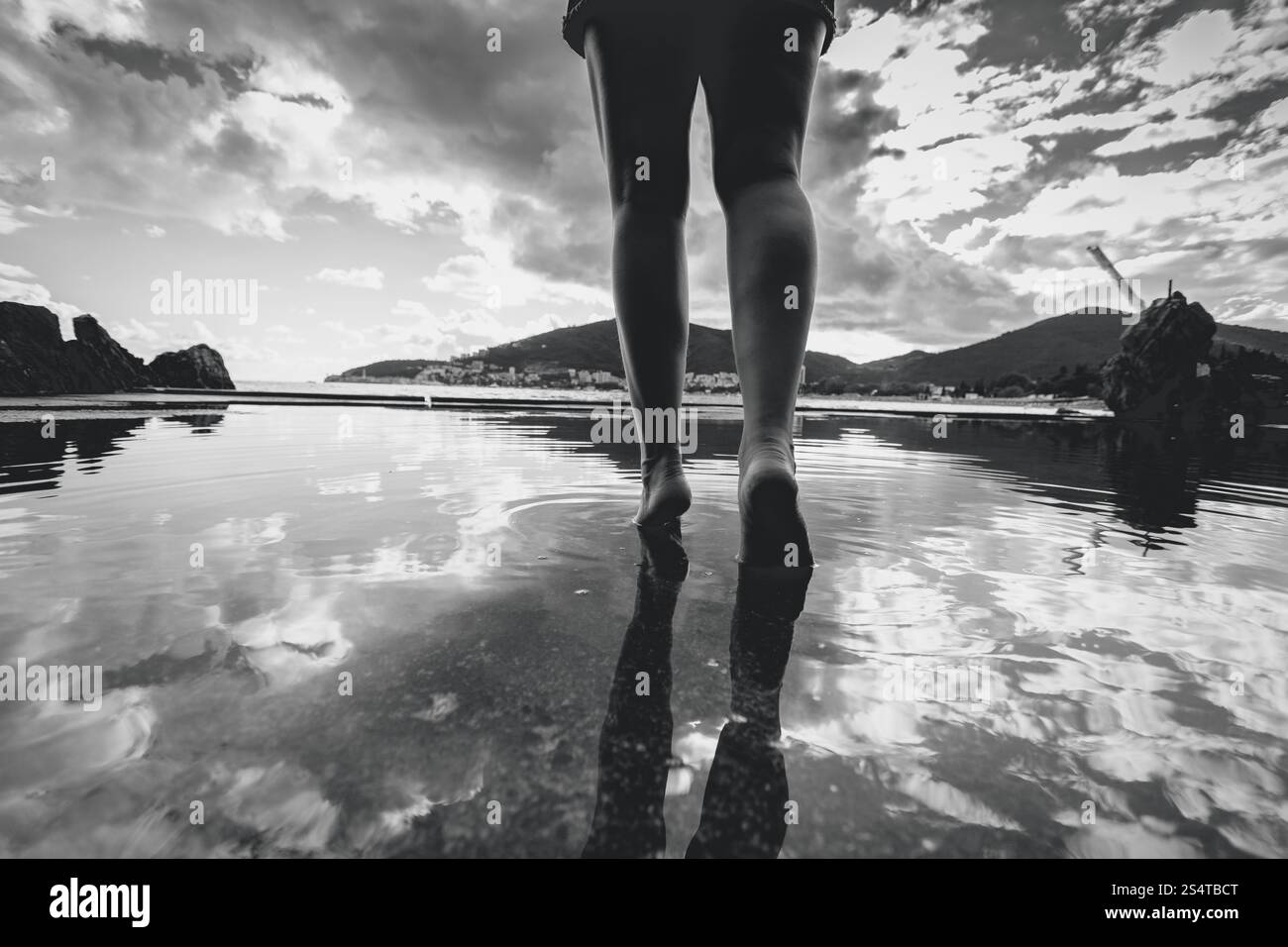 Photo en noir et blanc de femmes jambes marcher sur l'eau avec sky réfléchissant sur elle Banque D'Images