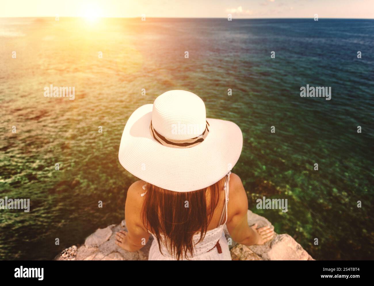 Photo gros plan de young woman wearing white hat en regardant le coucher du soleil sur la mer Banque D'Images