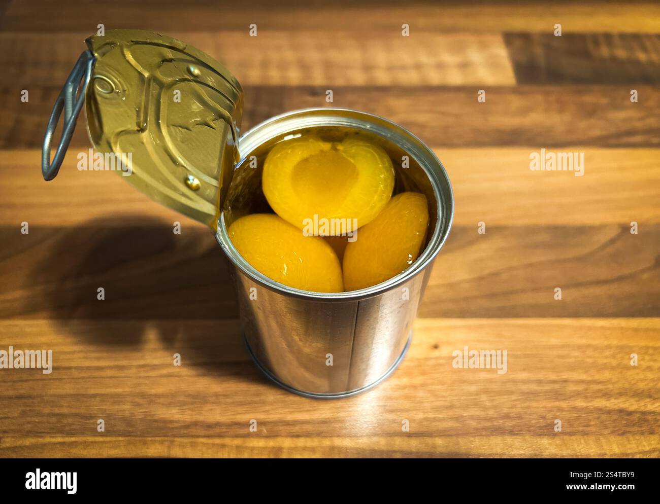 Berlin, Allemagne. 04th Dec, 2024. Une boîte de conserve avec des demi-pêches est ouverte sur une table en bois dans la cuisine. Le revêtement des boîtes contient du bisphénol A (BPA). Ce composé chimique peut être transféré au contenu et affecter le système hormonal humain lorsqu'il est consommé. Crédit : Soeren Stache/dpa/Alamy Live News Banque D'Images