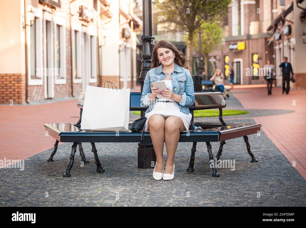 Belle femme avec tablet relaxing on bench after shopping Banque D'Images