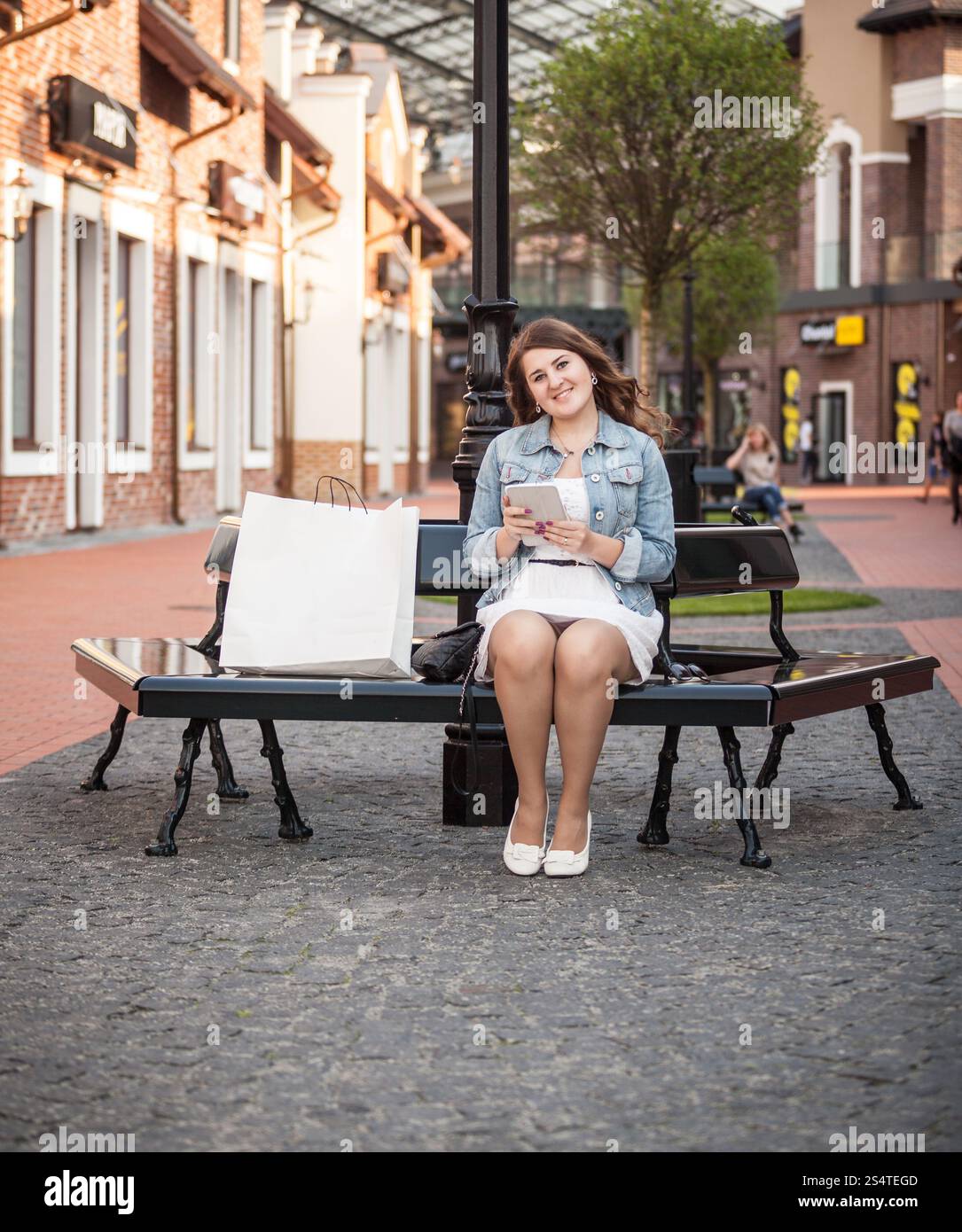 Beautiful woman sitting on bench with shopping bags and using tablet Banque D'Images