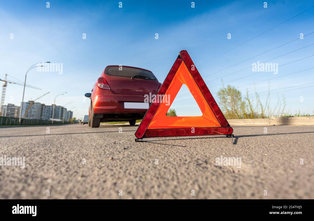 Photo Gros plan d'un triangle rouge sur la route à côté de la voiture cassée Banque D'Images