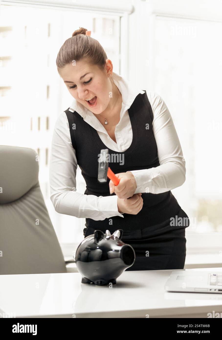 Portrait of angry businesswoman breaking piggy bank with hammer Banque D'Images