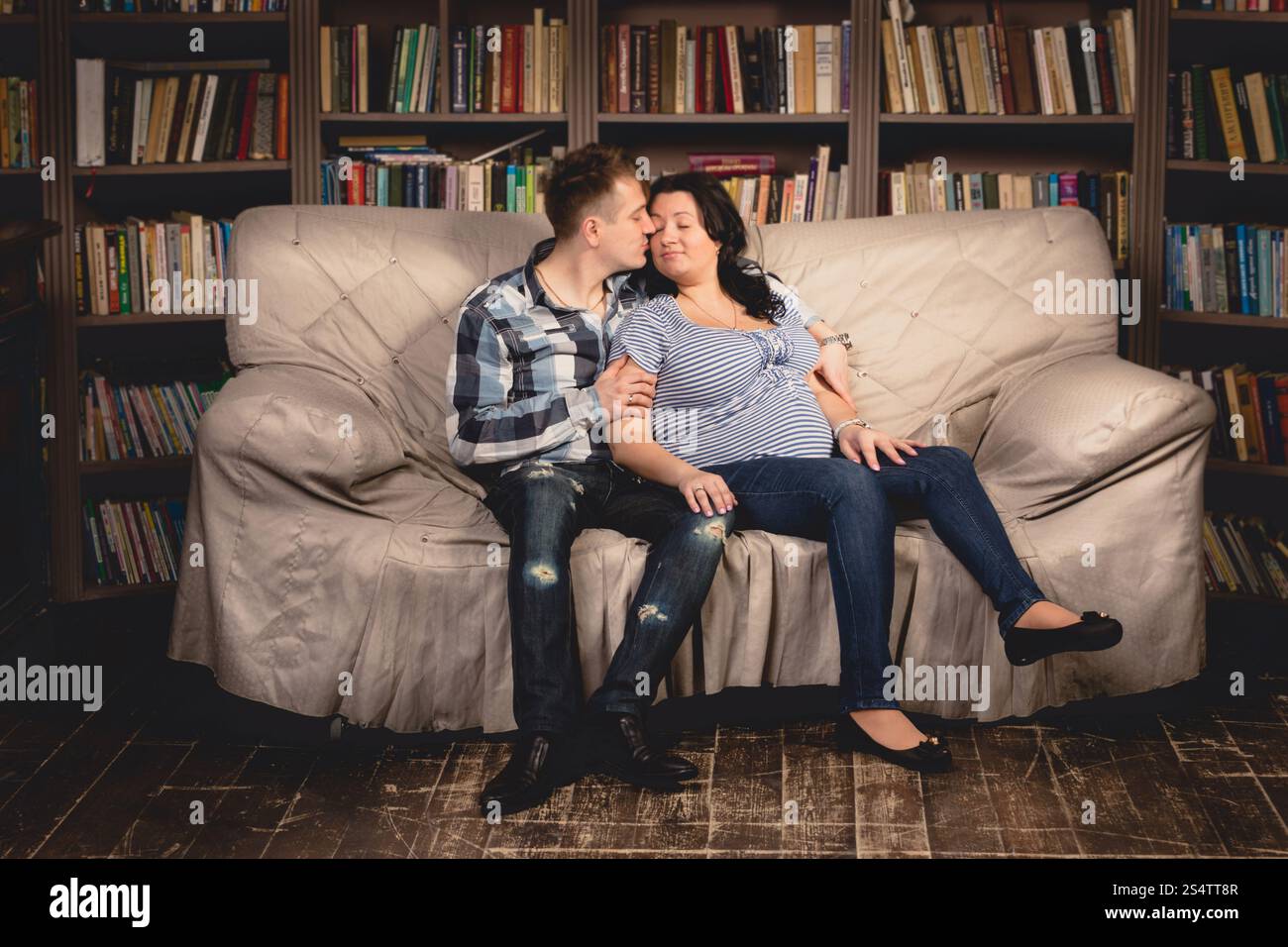 De belles jeunes femmes enceintes couple sitting on sofa contre étagères Banque D'Images