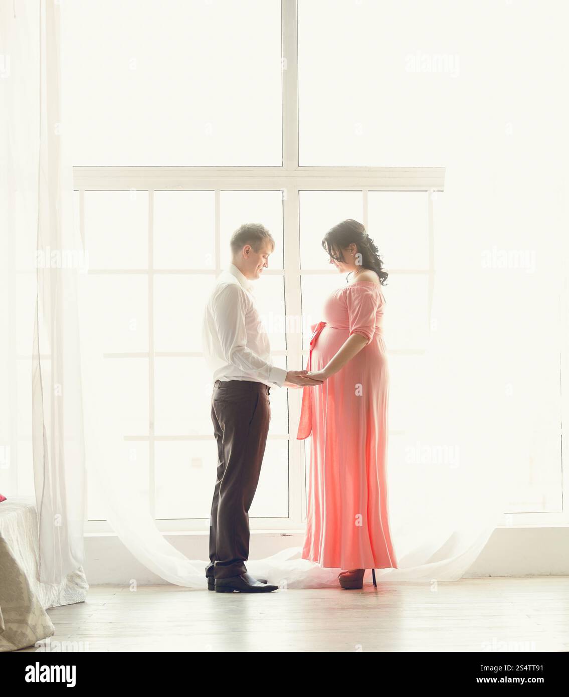 Photo de tons beautiful pregnant couple holding hands at grande fenêtre Banque D'Images
