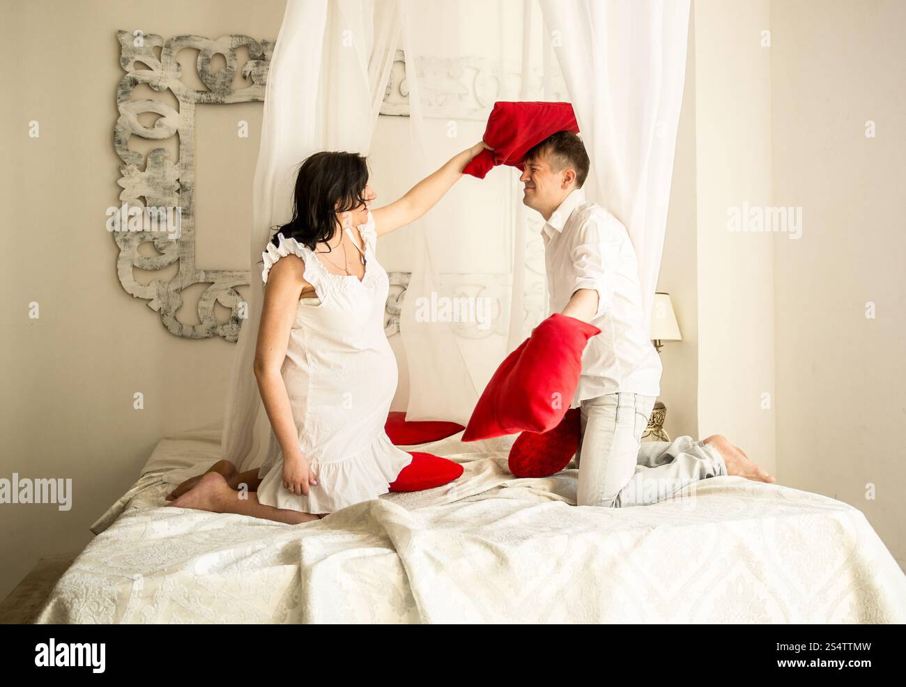 Happy pregnant couple having pillow fight sur beau lit Banque D'Images