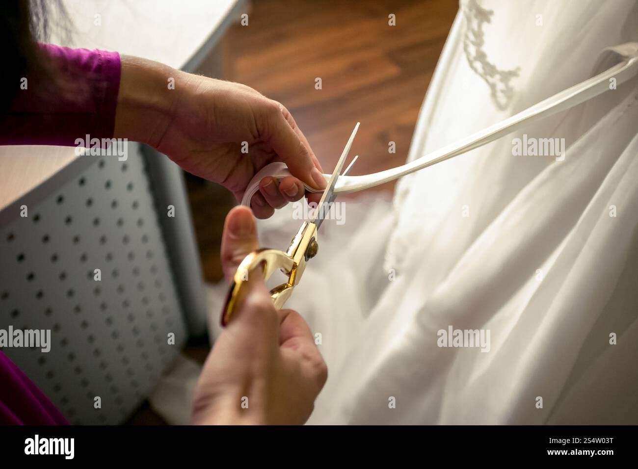 Gros plan du tailleur coupant le ruban sur la robe de mariée blanche Banque D'Images