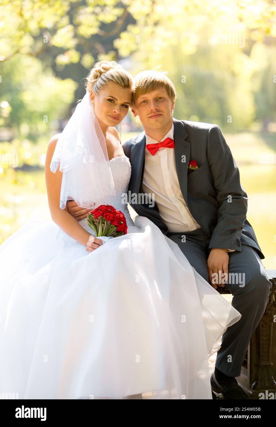 Portrait de mariée souriante et marié assis sur le banc à la rivière sous le grand arbre Banque D'Images