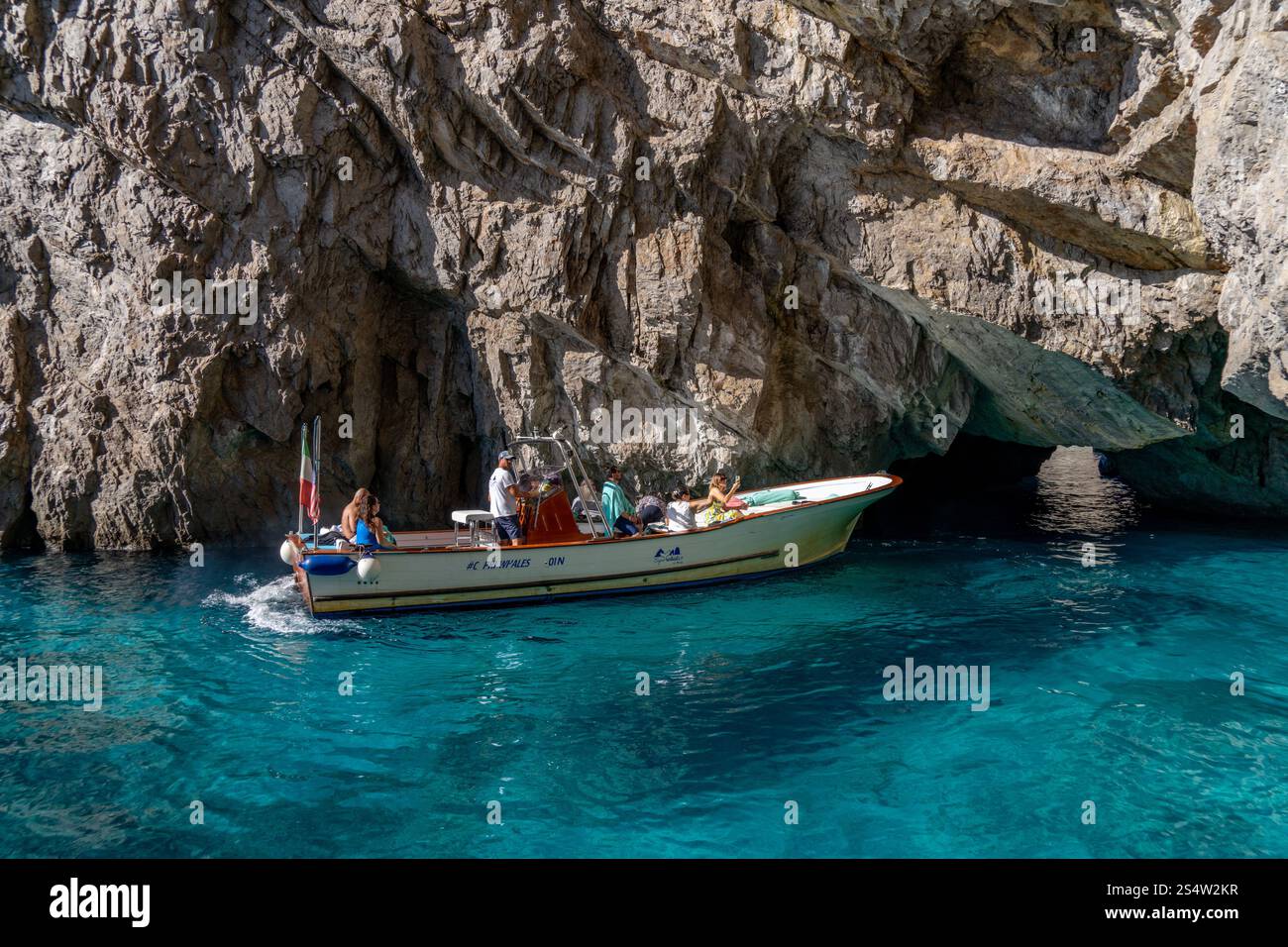 Les gens dans un bateau d'excursion dans l'eau verte claire par la Grotte verte sur la côte de l'île de Capri, Italie. Banque D'Images