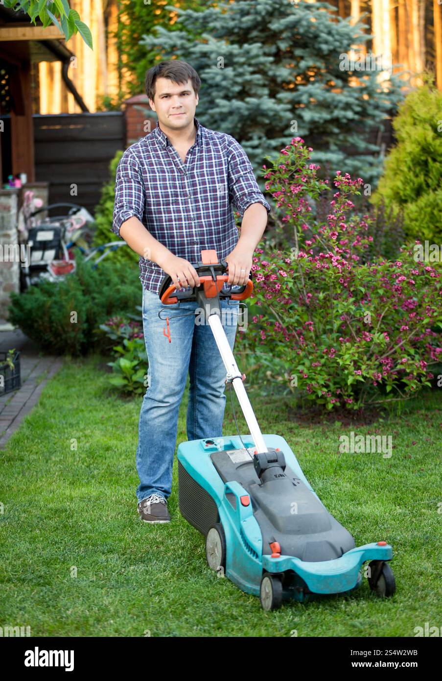 Beau jeune homme de la tonte de l'herbe à l'arrière-cour maison Banque D'Images