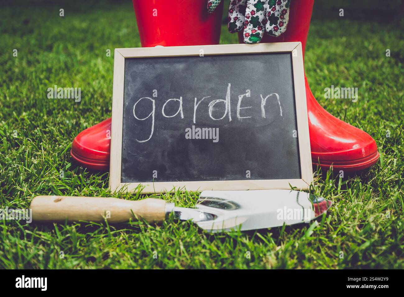 Photo rapprochée tonifiée d'un tableau noir avec le mot jardin 'couché sur l'herbe à côté des outils de jardin' Banque D'Images