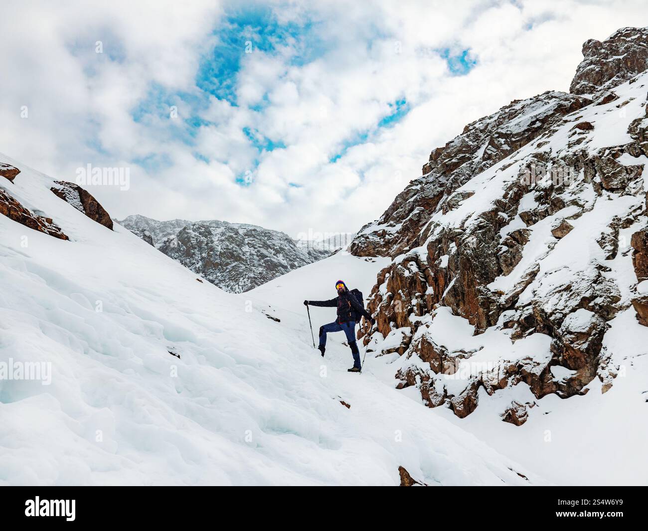 Un randonneur mâle haut dans les montagnes en hiver. Voyageur barbu avec un sac à dos debout sur une pente enneigée. Randonnée dans les montagnes d'hiver Banque D'Images