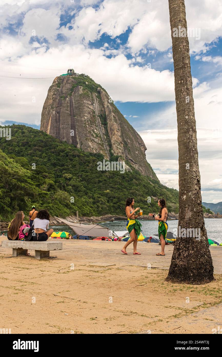 2 filles discutent à côté de Vermelha Beach avec Sugarloaf Mountain en arrière-plan, Rio de Janeiro, Brésil. Banque D'Images
