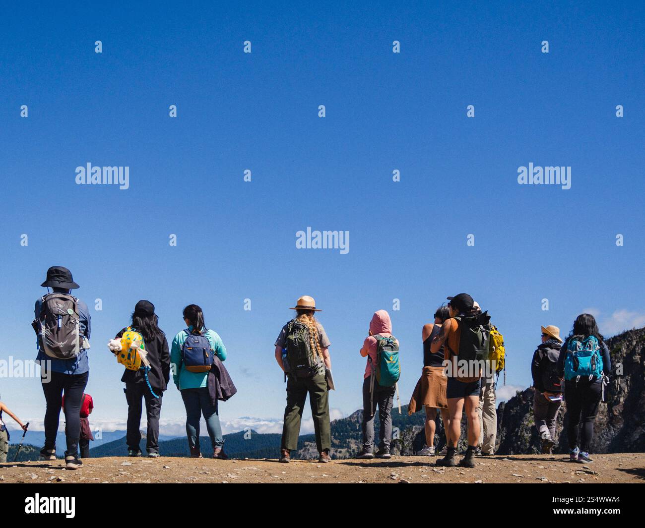Groupe d'Américains d'origine asiatique et un garde forestier portant des vêtements colorés, regardant au-dessus d'une crête à un sentier dans le parc national du Mont Rainier. Banque D'Images