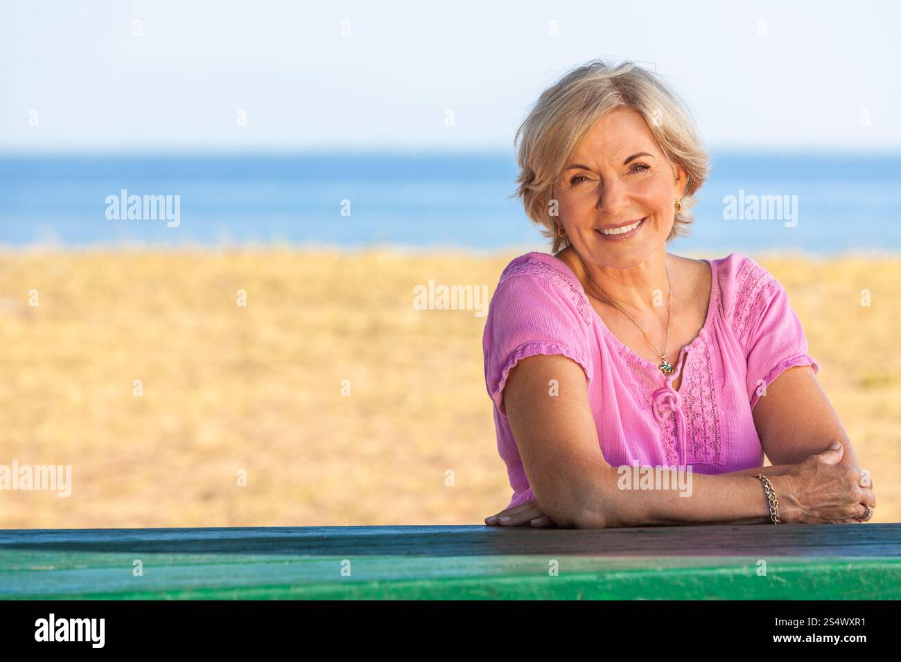 Portrait d'une femme senior élégante et attrayante assise à l'extérieur avec une plage et la mer derrière elle. Banque D'Images