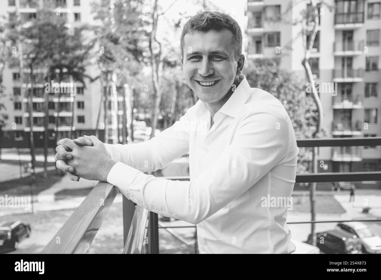 Portrait noir et blanc de l'homme souriant élégant en chemise blanche posant sur le balcon sur fond urbain Banque D'Images