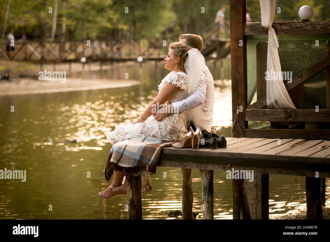Photo tonifiée d'un couple marié assis sur la jetée à la rivière et regardant le coucher du soleil Banque D'Images