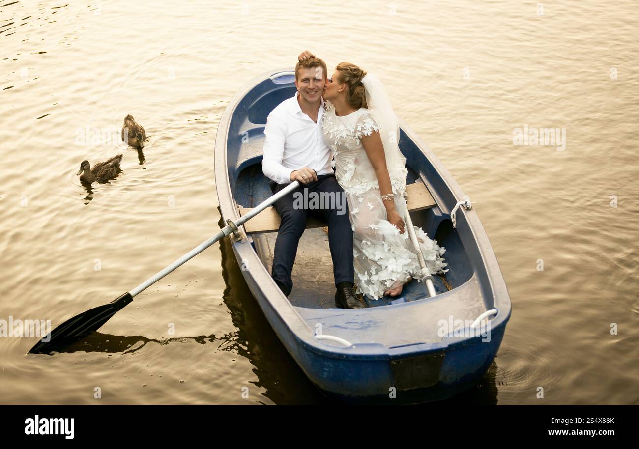 Belle mariée embrassant marié souriant tout en montant sur le bateau à rames Banque D'Images