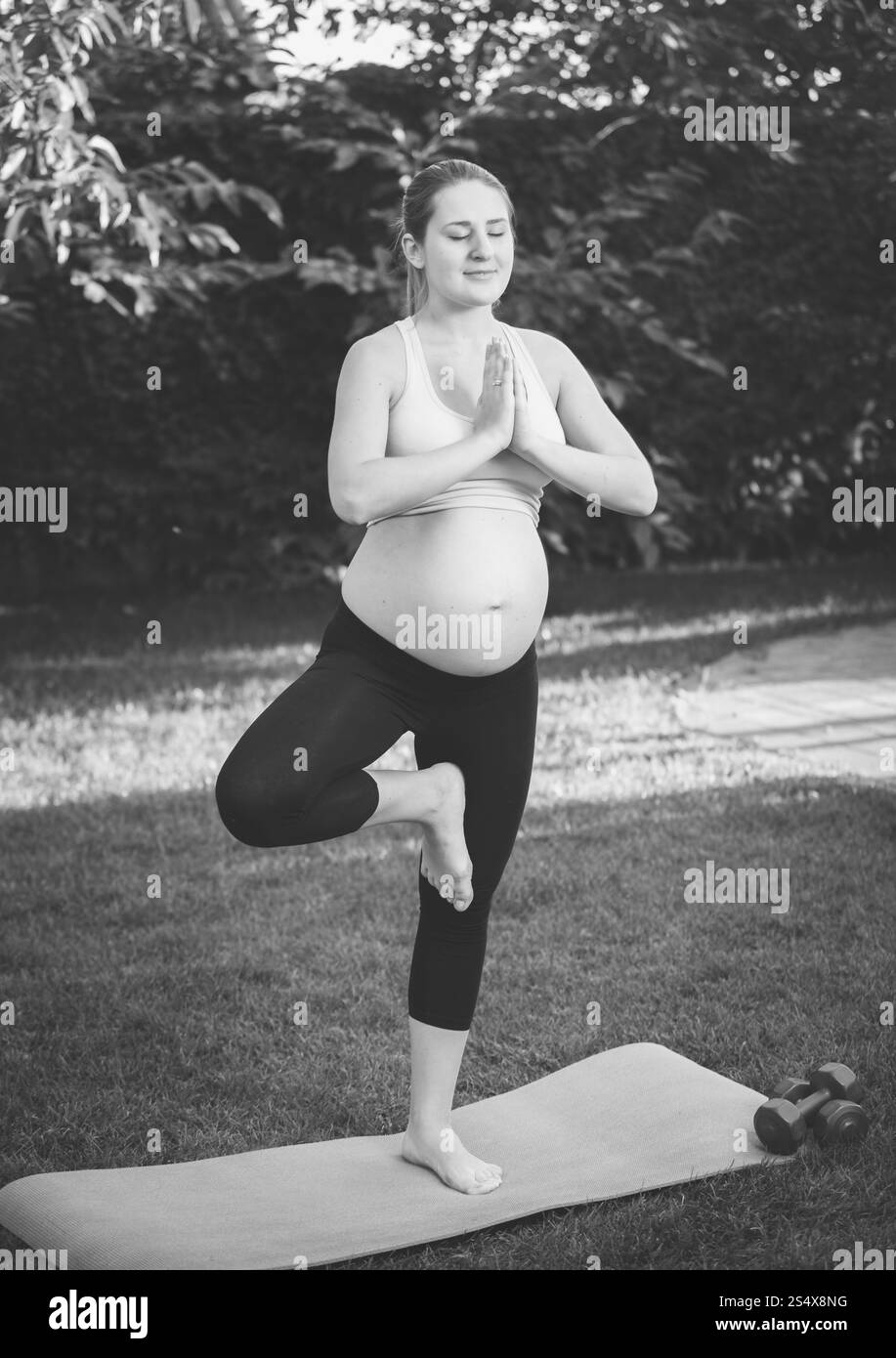 Tourné en noir et blanc de femme enceinte se tenant sur une jambe et la pratique du yoga at park Banque D'Images
