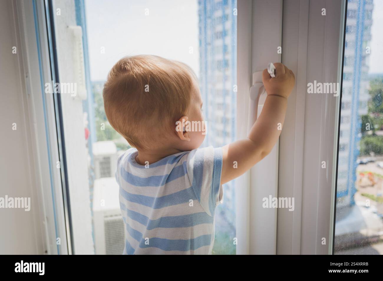 Portrait of cute baby boy tirant par la poignée de fenêtre. Concept de l'enfant en danger Banque D'Images