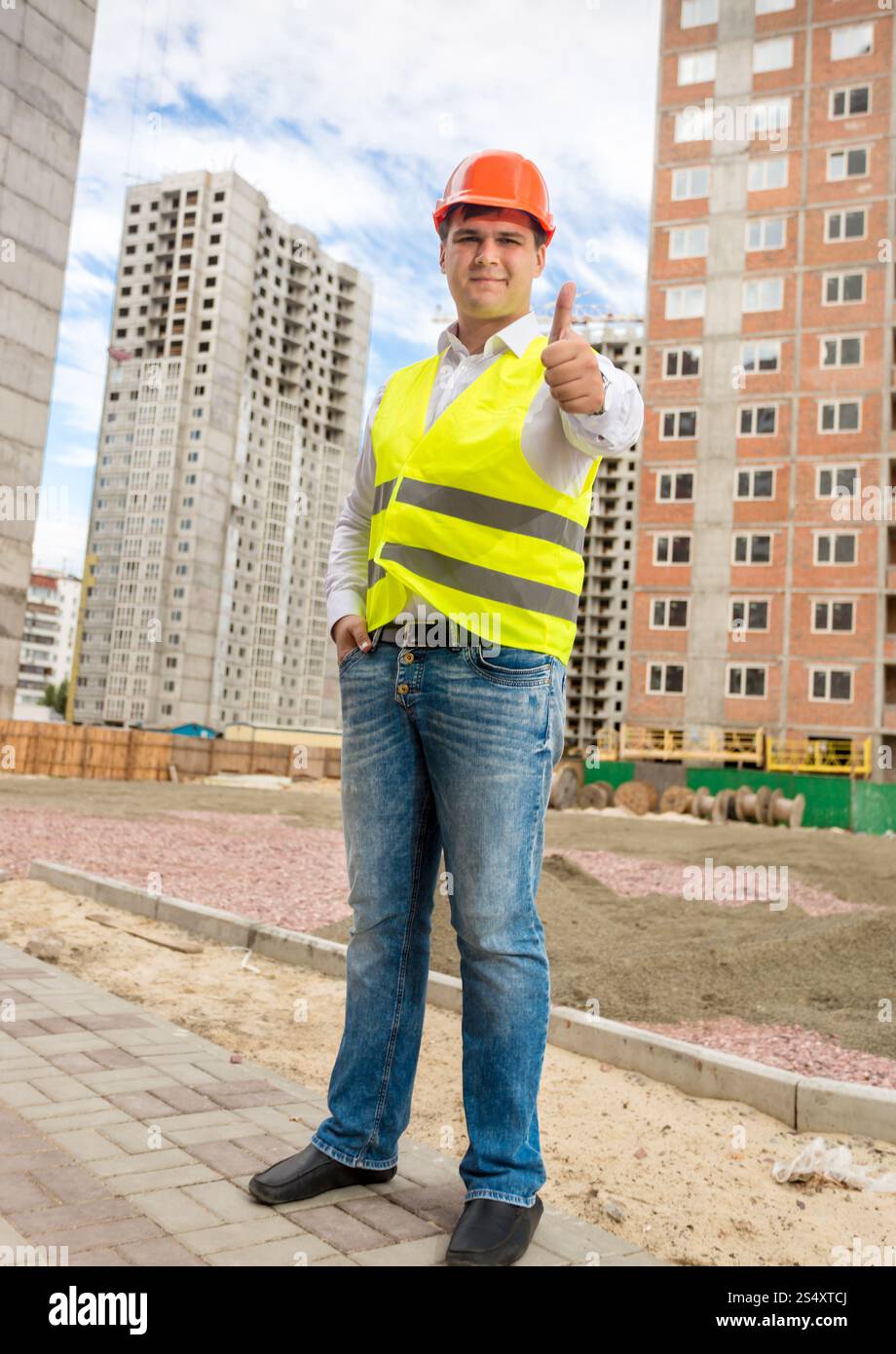 Jeune ingénieur en construction, souriant posant sur chantier avec thumb up Banque D'Images