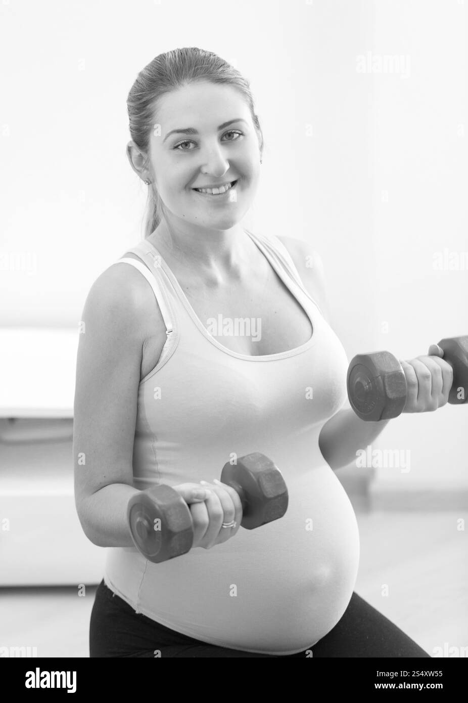 Le noir et blanc portrait of smiling pregnant woman exercising with dumbbells Banque D'Images