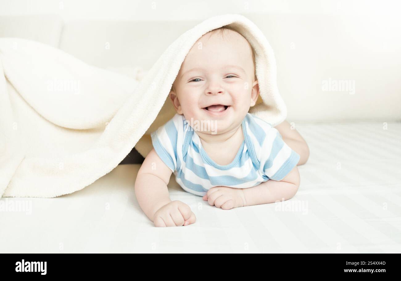 Rire mignon bébé 6 mois garçon couché sous la couverture sur le lit Banque D'Images