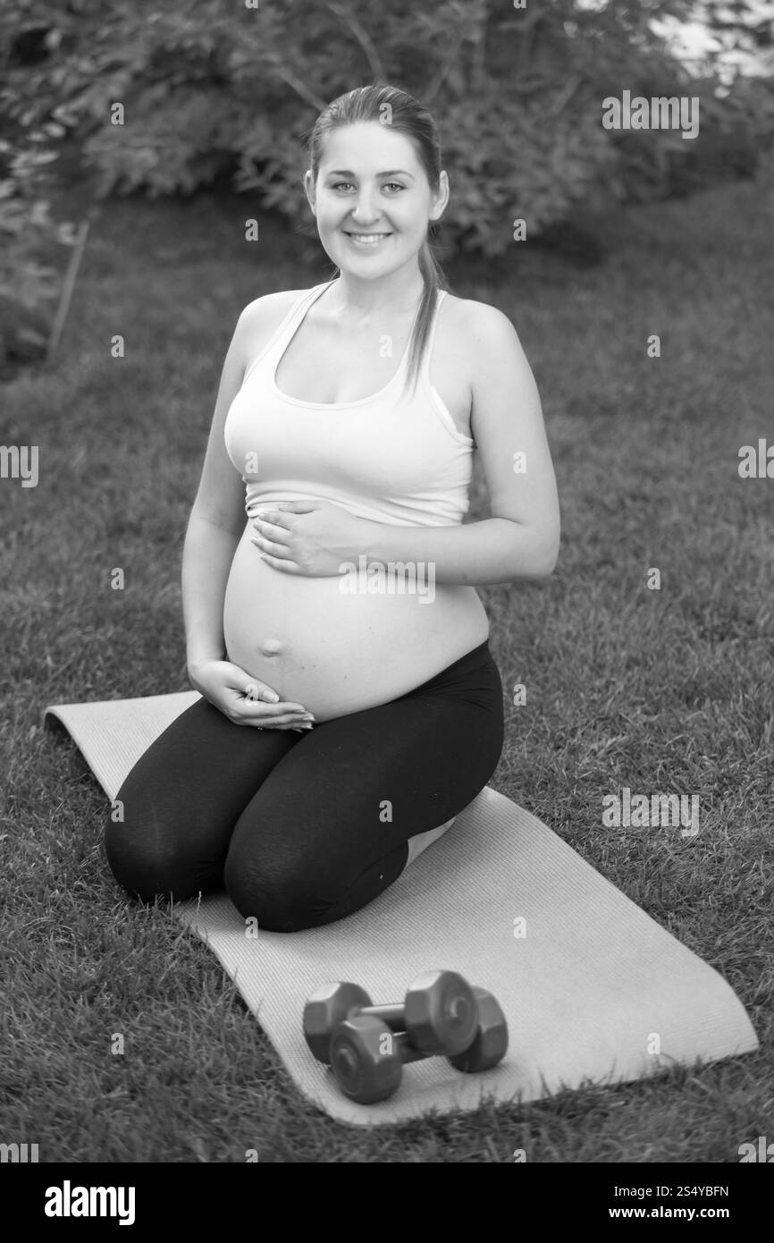 Femme enceinte noire et blanche assise sur les genoux au parc et tenant le gros ventre Banque D'Images