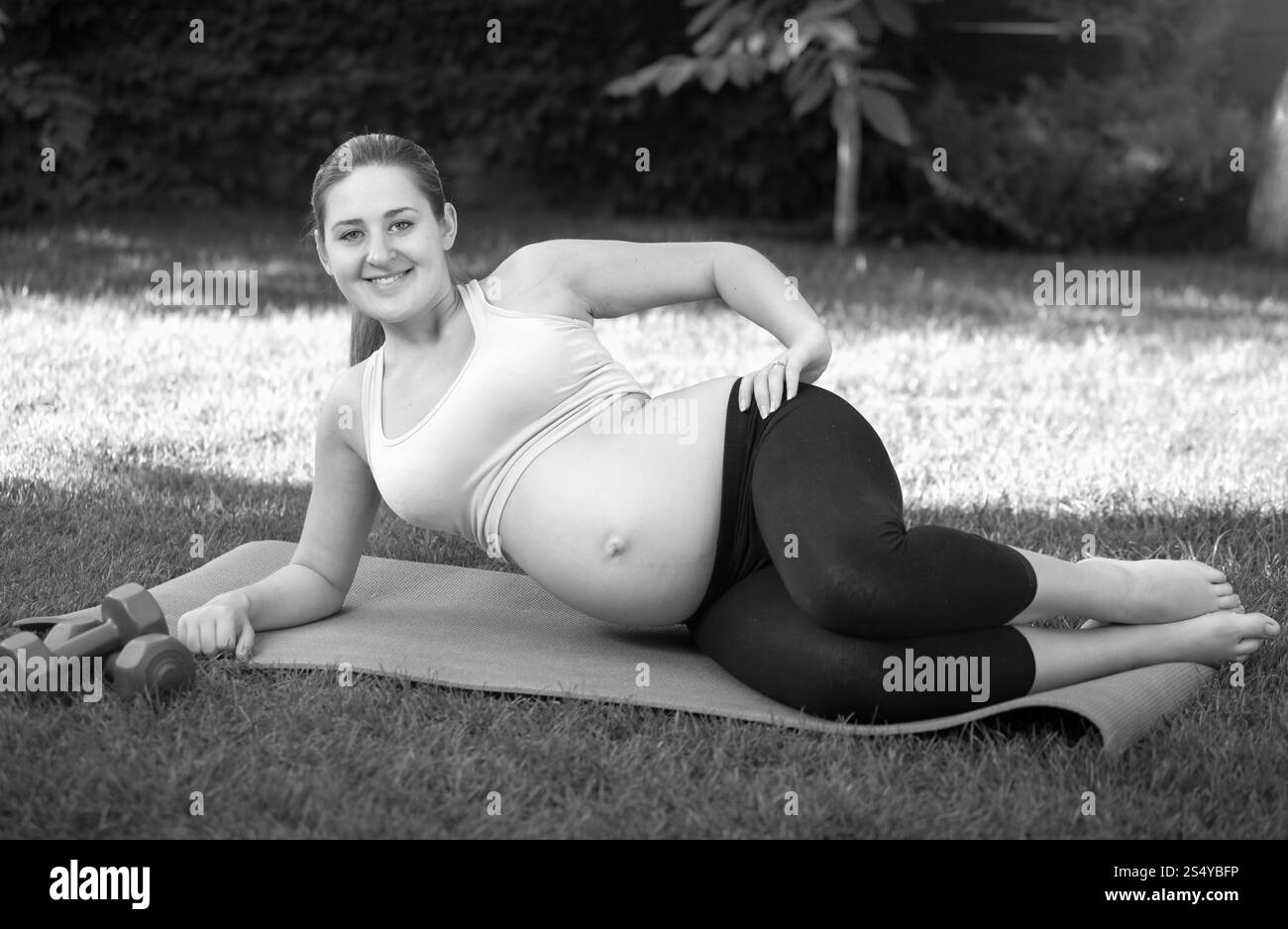 Image en noir et blanc d'une jeune femme enceinte qui s'étire avant le yoga sur l'herbe au parc Banque D'Images