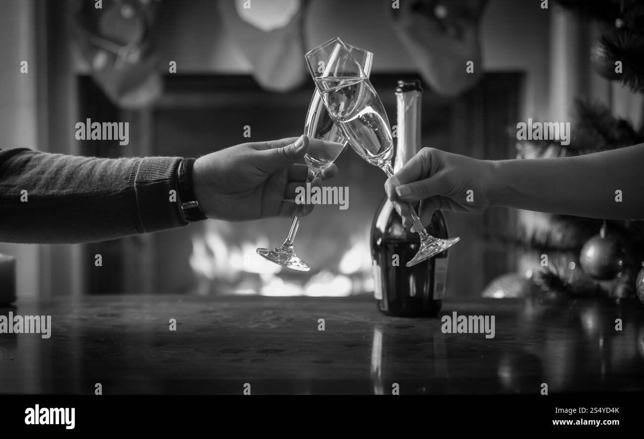 Gros plan de l'homme et de la femme célébrant Noël et clinking verres avec champagne à la cheminée. Fond de Noël monochrome Banque D'Images