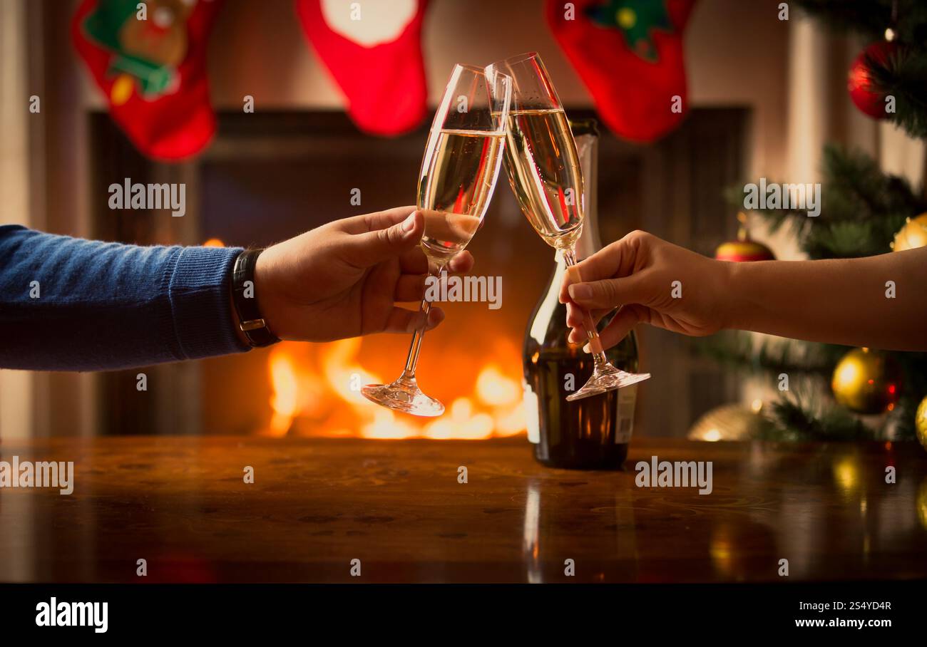 Mains masculines et féminines se tapissant avec des verres de champagne au salon décoré pour Noël Banque D'Images