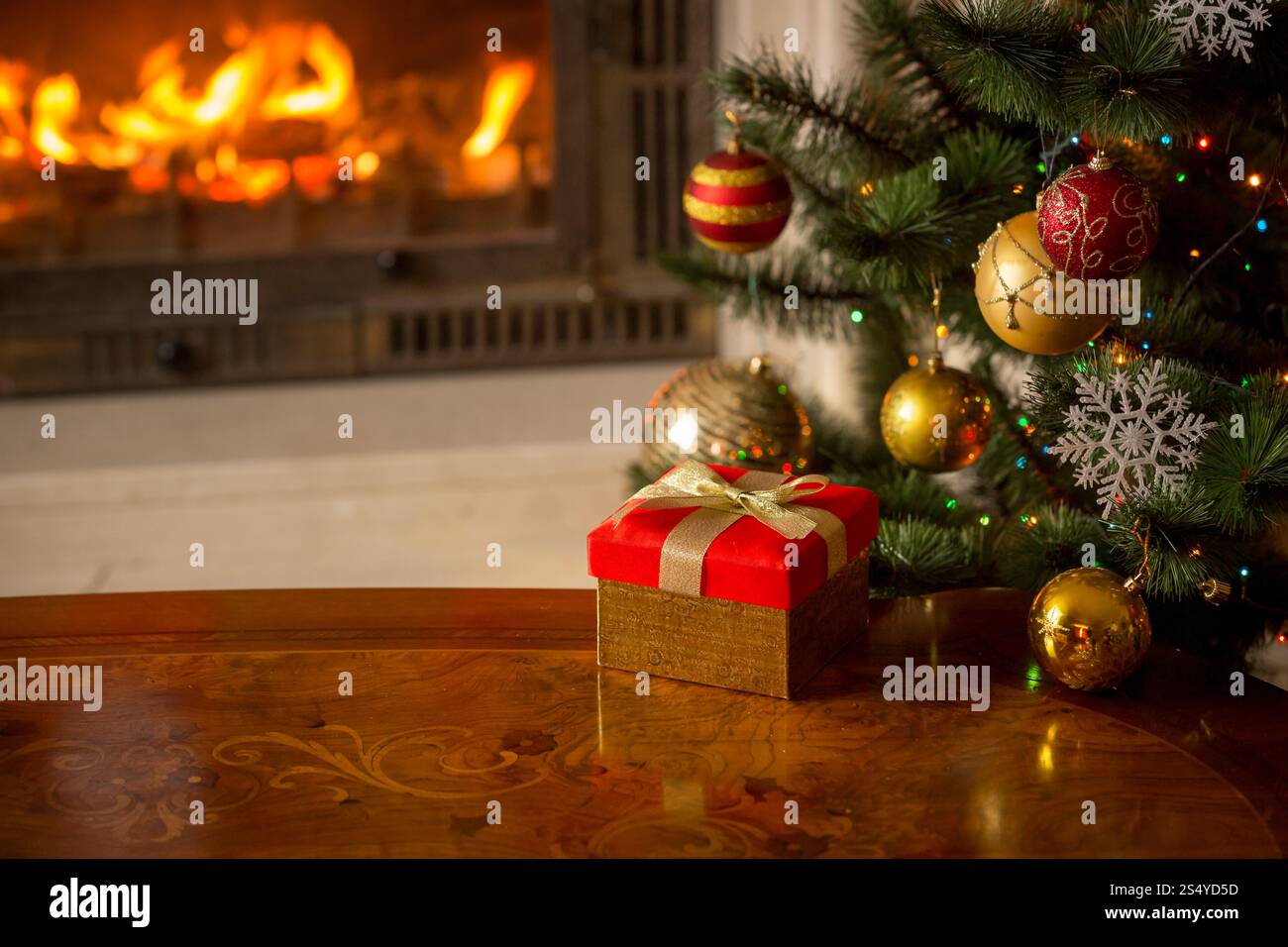 Gros plan image de boîte-cadeau rouge sur la table en bois devant la cheminée en feu et l'arbre de Noël. Espace vide pour le texte Banque D'Images