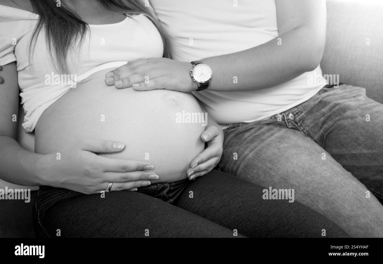 Gros plan photo noir et blanc d'un jeune homme tenant la main sur le ventre de femme enceinte Banque D'Images