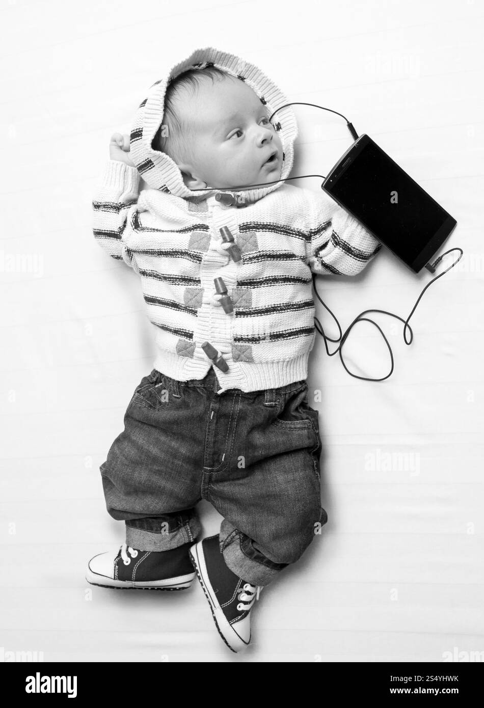Drôle de photo noir et blanc de bébé mignon écoutant de la musique sur le téléphone avec des écouteurs Banque D'Images